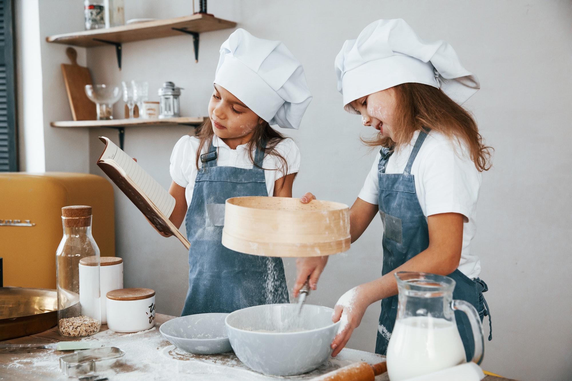 Two little girls preparing food by using sieve on the kitchen and reading receipt book